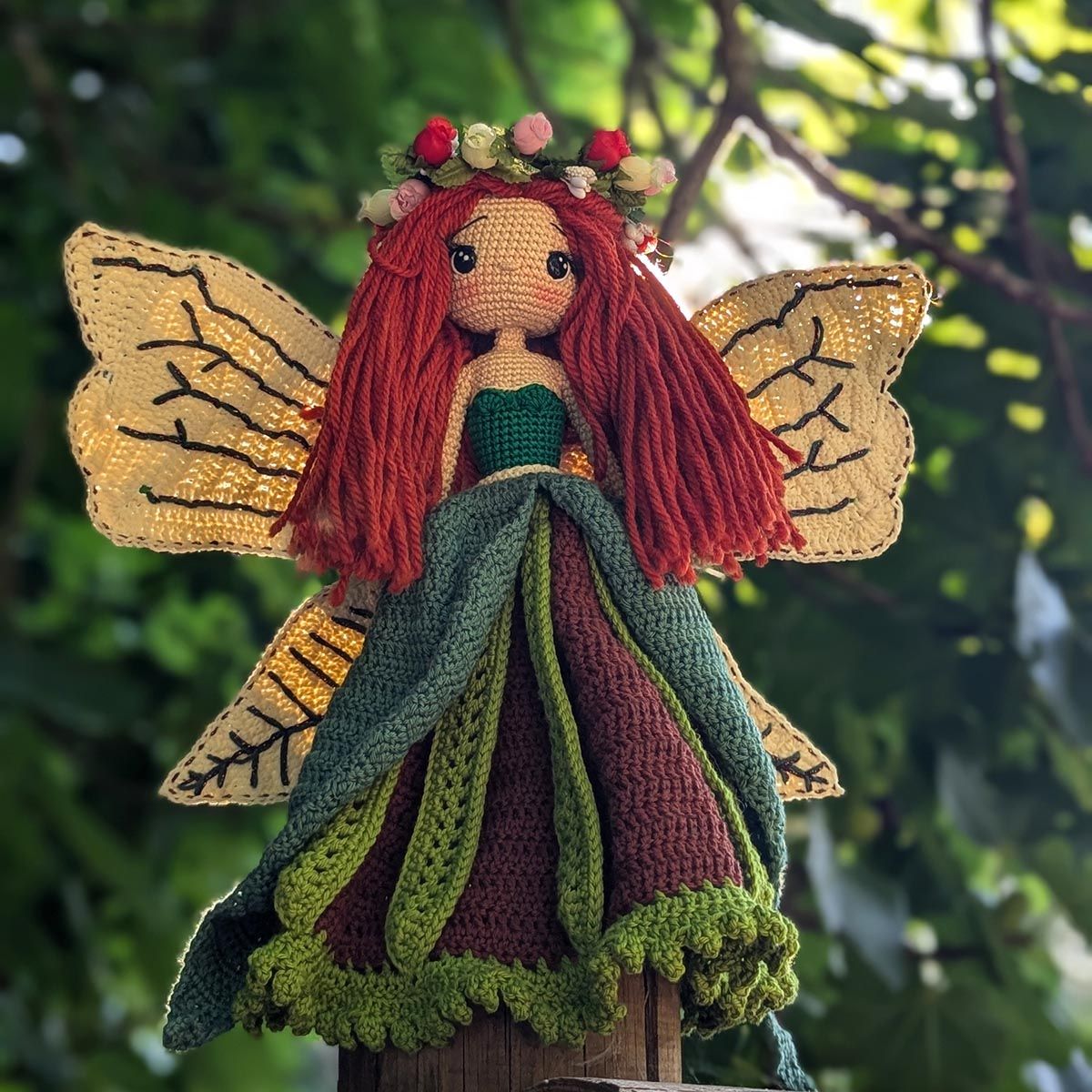 Alani Sauco, el Hada del Bosque, amigurumi con alas iluminadas y vestido verde y marrón entre la naturaleza
