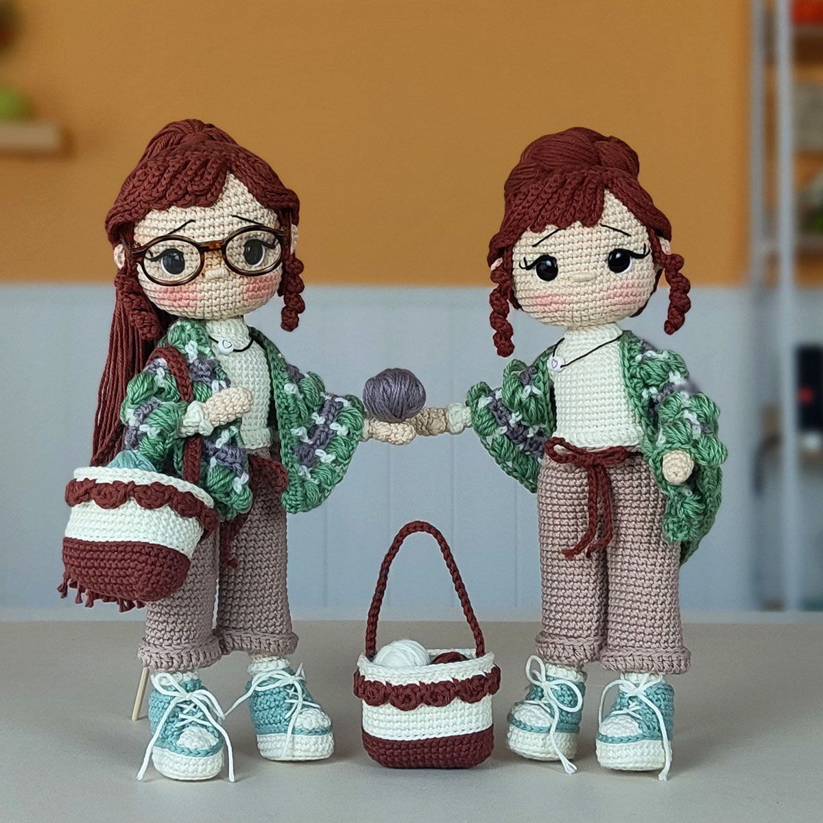 Muñeca amigurumi Nora Merino con chal verde y morado, bolso de crochet y zapatillas, sobre un fondo cálido.