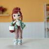 Muñeca amigurumi Nora Merino con chal verde y morado, bolso con ovillos y zapatillas, sobre un fondo mostaza.